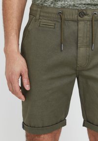 Shorts verts olive en tissu texturé, avec une taille à boutons et cordons de serrage, poche frontale et ourlet roulé.