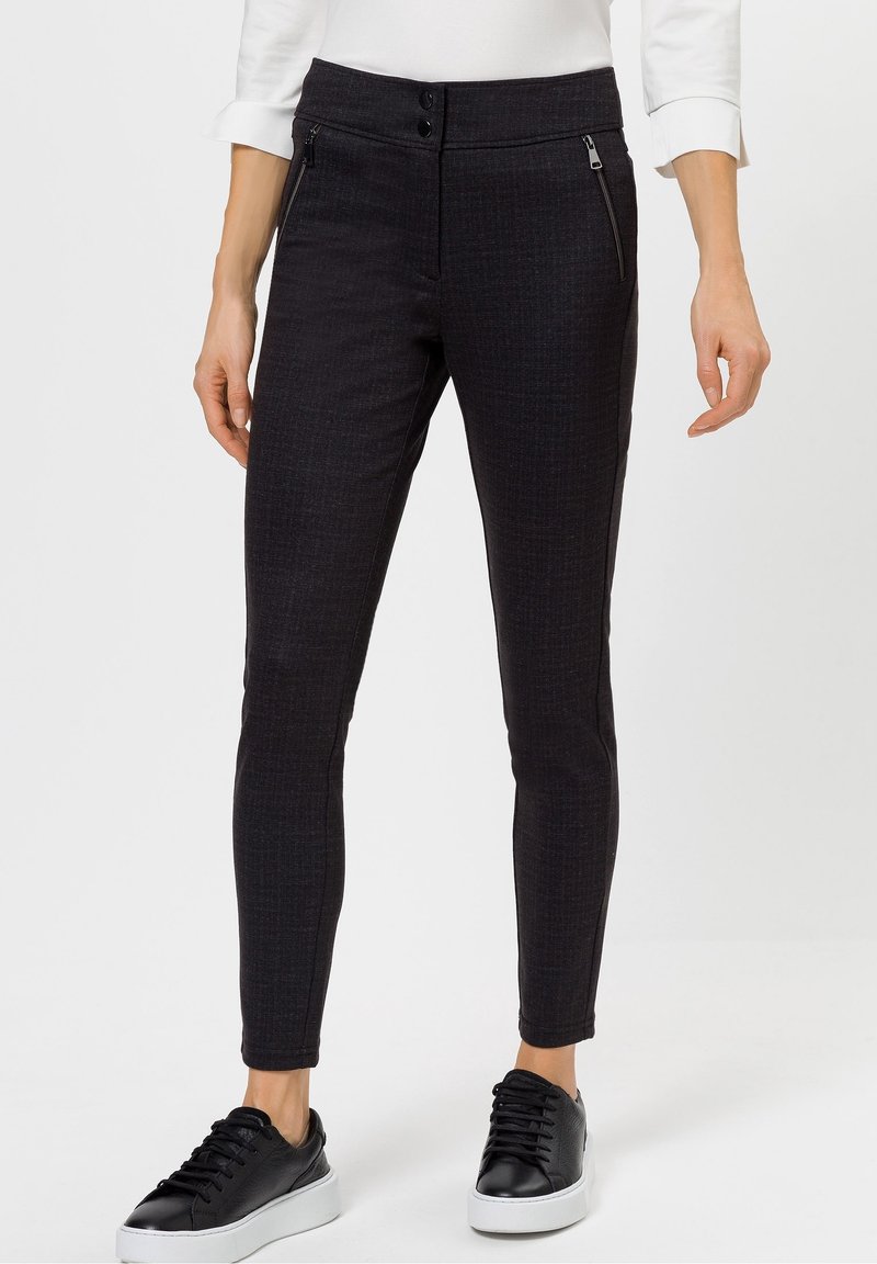 Pantaloni neri slim-fit con un motivo testurizzato, due cerniere frontali e una finitura liscia. Abbinati a sneakers nere e una maglietta bianca.