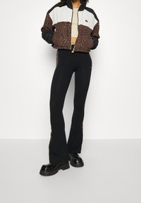 Leopardmönstrad bomberjacka med svarta ärmar och vit panel, tillsammans med svarta utsvängda leggings med matchande sidodetalj. Klumpiga svarta skor.