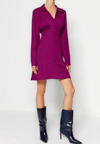 Fuchsiaklänning med krage, långa ärmar och rynkad detalj vid bysten. Matcher med knähöga, mörkblå stövlar med krokodilmönster.