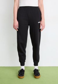 Zwarte jogpant met een ontspannen pasvorm, elastische tailleband, geborduurde enkels en witte logo details op de linkse heup. Zacht katoenmateriaal.