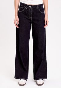 Mørkeblå vide denimbukser med hvid syning, frontlukning med knap og sidelommer.
