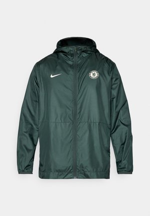 Zelená bunda Nike s predným zipsom, kapucňou a logom Chelsea FC na ľavej hrudi. Je vybavená elastickými manžetami a má hladkú textúru.