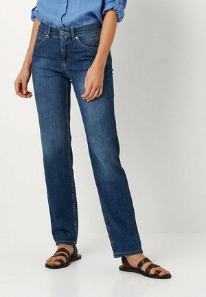 Dunkelblaue Jeans aus Denim mit geradem Bein, fünf Taschen und einem Knopfverschluss. Kombiniert mit braunen Sandalen mit Riemchen.