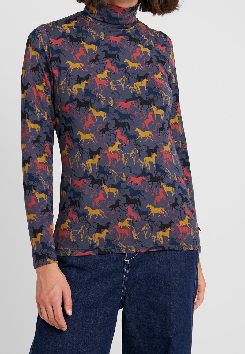 Långärmad tröja med hög krage tillverkad av stretchigt material, med en marinblå bakgrund och färgglada hästsilhuetter i röd, gul och svart.