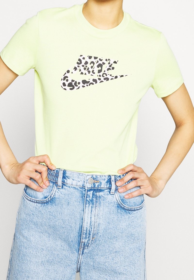 Limegrön bomullströja med ett leopardmönstrat Nike-logga, rund hals, korta ärmar och matchad med ljusblå jeans.