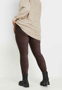 Brązowe legginsy z korduroju widoczne z tyłu, zestawione z długim beżowym swetrem w cętki. Widoczne są czarne botki za kostkę z detalami w postaci klamry.