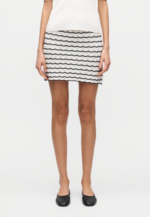 Mini-jupe à motif ondulé en crème avec des lignes bleu marine, en maille texturée avec un ourlet festonné. Associée à des ballerines noires.