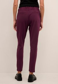 Pantalon maroon fuselé avec une taille élastique et deux poches arrière, confectionné dans un tissu extensible, associé à des chaussures noires à semelles épaisses.