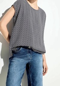 Top corto a maniche corte con motivo in bianco e nero abbinato a jeans di denim azzurri. Il top presenta una vestibilità comoda e un collo rotondo.