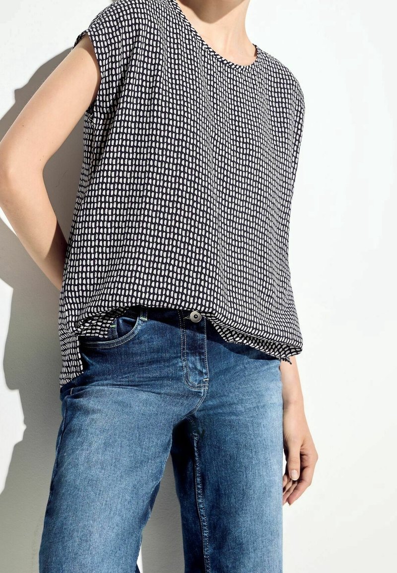 Top corto a maniche corte con motivo in bianco e nero abbinato a jeans di denim azzurri. Il top presenta una vestibilità comoda e un collo rotondo.