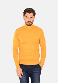 Maglione a collo alto arancione realizzato in un morbido tessuto, design aderente con maniche lunghe, abbinato a jeans blu scuro.