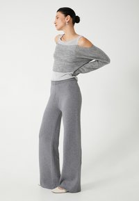 Grå strikket off-shoulder sweater lagdelt over en lysere grå top, parret med brede grå bukser. Glat overflade med blød finish.