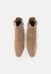 Paire de bottines en daim marron clair avec bouts pointus et fermetures éclair latérales, vues de dessus sur fond blanc.