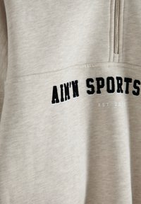 Sudadera de color beige claro con diseño de cremallera de cuarto, texto bordado en negro "AIM'N SPORTS" y año de creación "EST. 2013" debajo. Textura suave.