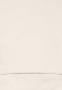 Tela de sudadera color crema con textura suave y dobladillo acanalado. Diseño liso sin patrones ni detalles visibles.