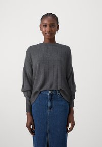 Maglione grigio a coste con scollo rotondo e spalle dropped, abbinato a una gonna in denim blu aderente con uno spacco frontale.