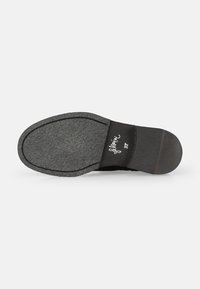Suela negra de zapato con fondo gris texturizado, diseño plano y un leve tacón. Presenta el nombre de la marca impreso en blanco en la plantilla.