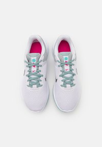 Un paio di scarpe da ginnastica bianche e grigie con lacci turchesi e solette rosa brillante viste dall'alto su uno sfondo bianco.