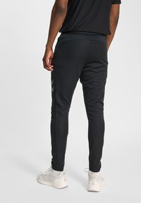 Schwarze athletische Jogginghosen mit schlanker Passform, elastischem Bund und reflektierenden seitlichen Akzenten. Kombiniert mit hellen Sportschuhen.