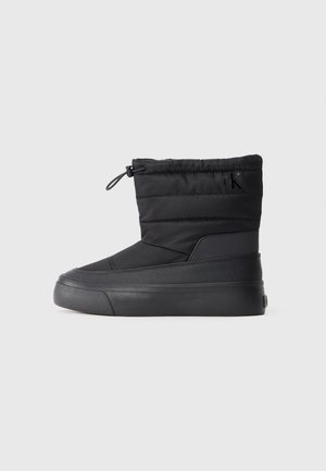 Botte d'hiver noire mi-mollet avec dessus matelassé, fermeture à cordon en haut, semelle texturée et logo discret "cK" près de la cheville.