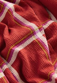 Tessuto rosso texturizzato con superficie increspata, caratterizzato da un motivo a quadri con strisce rosa, bianche e verdi che accentuano il design.