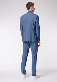 Helles blaues Outfit mit maßgeschneidertem Design, bestehend aus einem einreihigen Sakko und schmal geschnittenen Hosen, kombiniert mit weißen Sneakers.