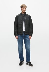 Czarna skórzana kurtka z kieszenią na zamek na klatce piersiowej, z prążkowanymi akcentami na ramionach, w połączeniu z niebieskimi dżinsami i czarnymi sneakersami. Pod spodem biała koszulka.