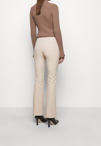 Un pull col roulé côtelé marron associé à un pantalon évasé beige clair et des chaussures à talons hauts noires, présentant une texture lisse et un minimum de détails.