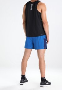 Camiseta sin mangas negra con "BERLÍN" en texto blanco, combinada con pantalones cortos deportivos azules con un acento en azul marino. Zapatillas de correr negras.