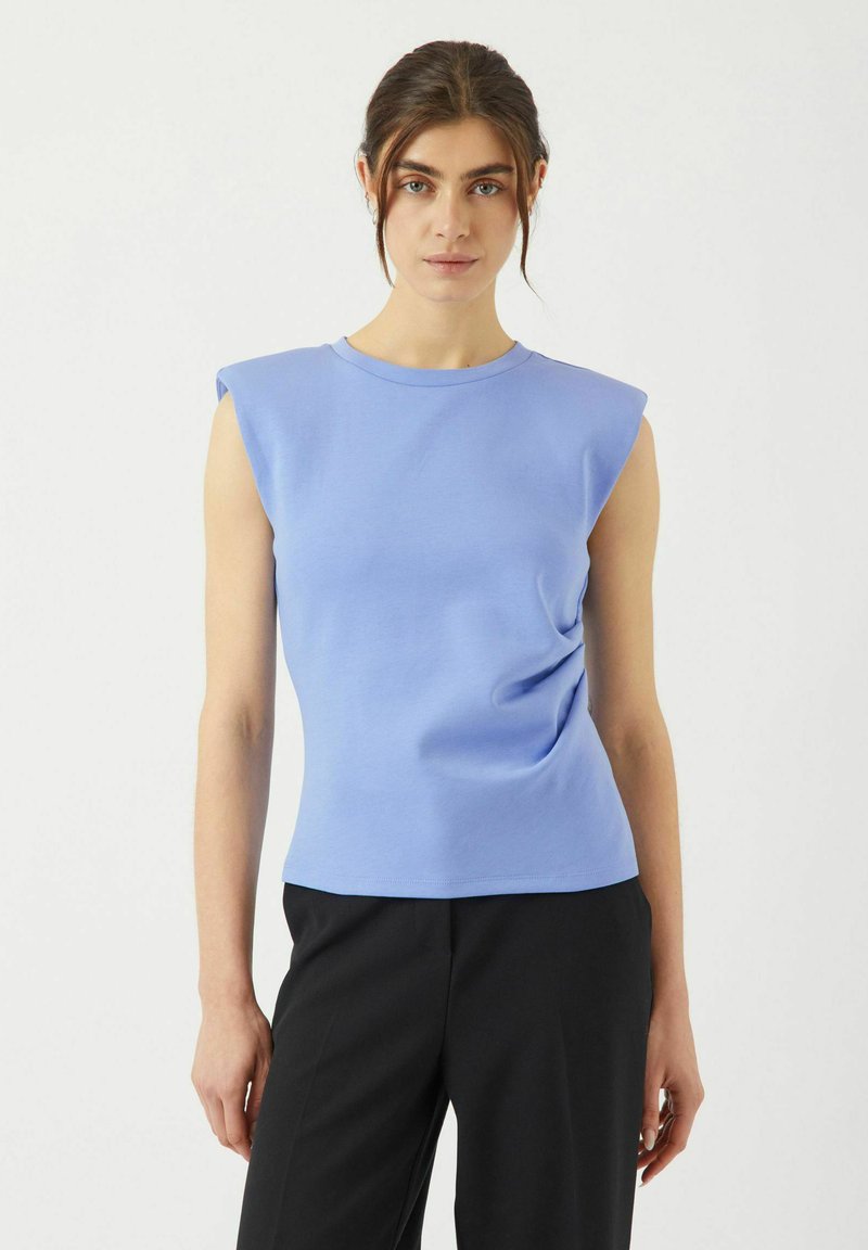 Ljusblå kortärmad topp med rund halsringning och strukturerad axeldesign. Samlat detalj vid midjan, i kombination med svarta byxor.