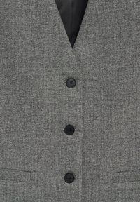 Gilet gris en tweed avec trois boutons noirs et une doublure intérieure en forme de V noire visible au col.