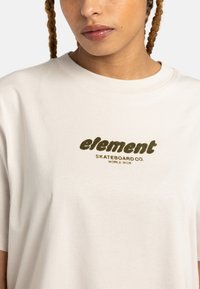 Kremowa bawełniana koszulka z krótkim rękawem z zielonym graficznym logo "element" oraz napisem "SKATEBOARD CO. WORLD WIDE" w casualowej czcionce.