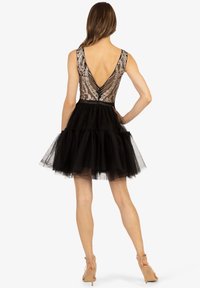 Robe en tulle noire avec un corsage transparent ajusté et un dos en V, ornée de décorations florales et d'une jupe à plusieurs couches.