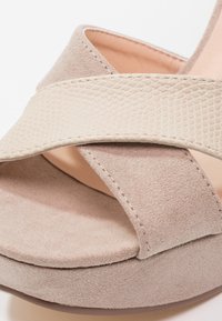Gros plan sur une sandale compensée en daim beige avec une bride texturée traversant le devant de la semelle.