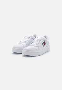 Zapatillas blancas con acabado de cuero liso, punta redondeada, diseño con cordones, detalles perforados y un sutil logo en el lateral.