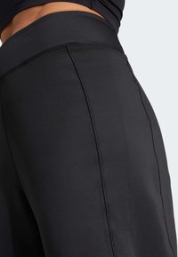 Čierne športové legíny s vysokým pásom, hladkou textúrou a viditeľným detailom švov po stranách.