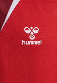 Tissu rouge avec un logo d'abeille stylisée blanche au-dessus du mot « hummel » imprimé en lettres minuscules.