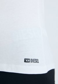 Biely bavlnený tričko s čiernym logom "DIESEL" blízko lemu, s hladkou textúrou a jednoduchým dizajnom.