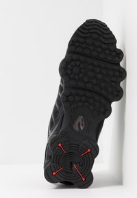 Μαύρη σόλα αθλητικού παπουτσιού με υφή ελαστικού αντιολισθητικού, που διαθέτει κυκλικά και τριγωνικά μοτίβα, τονισμένη με κόκκινα κυκλικά μεταλλικά στοιχεία.