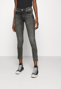 Jeans negros ajustados y recortados con un acabado descolorido, que cuentan con una cintura alta, bolsillos frontales y detalle de botón adornado, combinados con zapatillas negras.