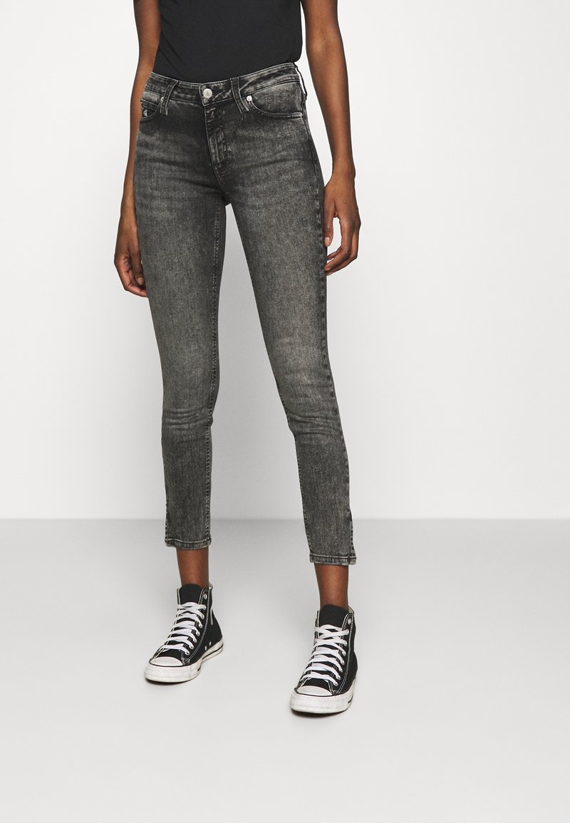 Jeans negros ajustados y recortados con un acabado descolorido, que cuentan con una cintura alta, bolsillos frontales y detalle de botón adornado, combinados con zapatillas negras.