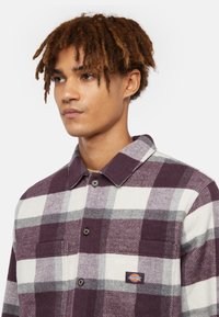 Flannel skjorte i lilla, hvid og grå tern. Har knaplukning foran, krave og en brystlomme med et Dickies-logo. Tekstureret stof.