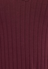 Haut en tricot bordeaux marle avec une texture à côtes verticales, dotée d'un col en V. Le tissu est lisse et extensible.