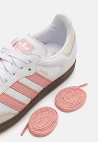 Vit lädersneaker med rosa detaljer och tre ränder, rund tå, texturerad brun gummisula och två matchande rosa skosnören.