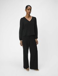 Zwarte wijde broek in combinatie met een zwarte top met V-hals en lange, gathered mouwen. Glad materiaal, minimalistisch ontwerp en geen zichtbare patronen.