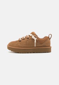 Braune Wildleder- und Mesh-Sneaker mit einer dicken Gummisohle, cremefarbenen Schnürsenkeln und einem Schlaufen-Tag an der Ferse. Besitzt ein niedriges Profil und strukturierte Akzente.