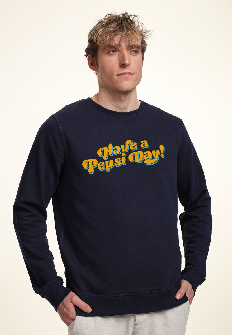 Sudadera azul marino de manga larga, con cuello redondo, y un gran gráfico amarillo y turquesa que dice "¡Ten un día de Pepsi!" en la parte frontal.
