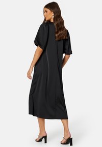 Czarna satynowa sukienka o luźnym kroju, z krótkimi bufkami i długości midi. Posiada subtelny blask oraz kieszenie po bokach.