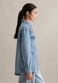 Lichtblauw denim overhemd met een knoopsluiting aan de voorkant, lange mouwen en een enkele borstzak, gedragen met bijpassende denim broek.